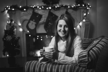 Black and white portrait of smiling woman drinking tea at fireplace at Christmas