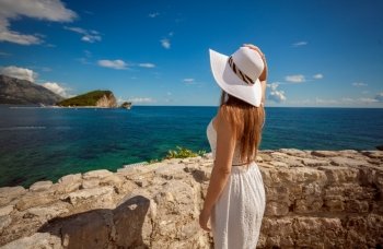 Beautiful young woman standing on top sea shore and looking at island at sea