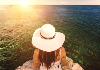 Closeup photo of young woman wearing white hat looking at sunset over the sea