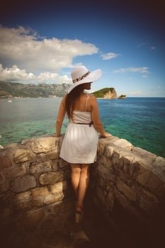 Beautiful young woman wearing white hat looking at far away island at sea