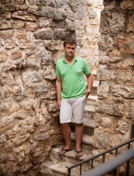Young man in shorts leaning against ancient stone wall
