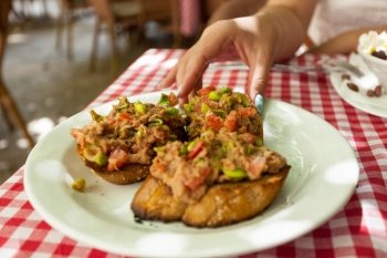 Closeup photo of woman taking bruschetta with tuna from plate at restaurant