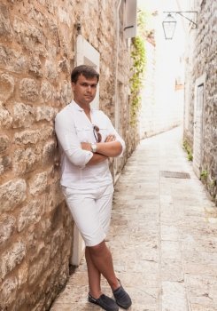 Handsome stylish man leaning against old stone wall on street