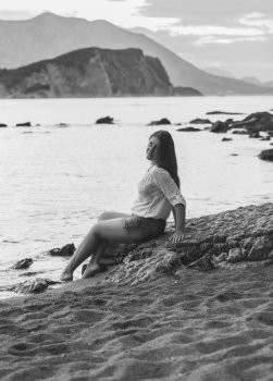 Black and white photo of sexy woman sitting on rock at deserted beach