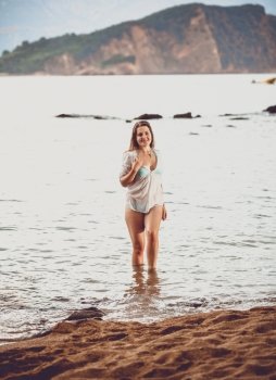 Beautiful young woman in white shirt walking out of sea on beach