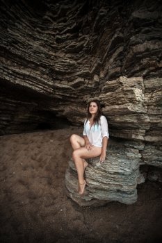Beautiful slim woman sitting on big cliff at sea cave