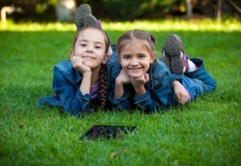 Closeup portrait of two little girls lying on grass with tablet