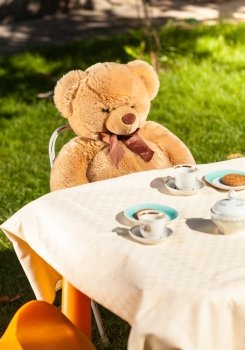 Big teddy bear sitting behind table and drinking tea