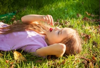 Beautiful young girl lying on grass and eating cherry outdoor