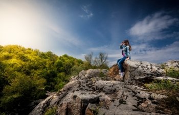 Photo of beautiful woman sitting on top of cliff and looking at sunset