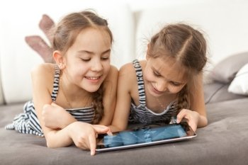 Closeup portrait of two smiling girls lying on couch and using tablet