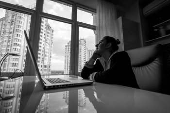 Black and white portrait of dreamy businesswoman looking out of window in office