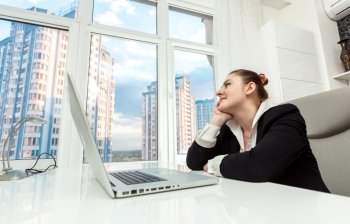 Portrait of young businesswoman sitting behind table and looking out of window