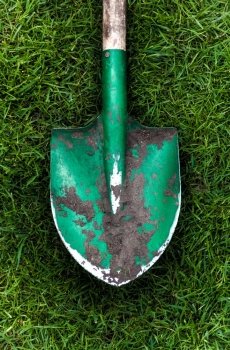 Closeup photo of green shovel with soil on grass