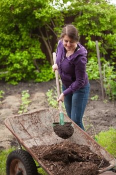 Photo of woman fertilizing garden bed with compost from wheelbarrow