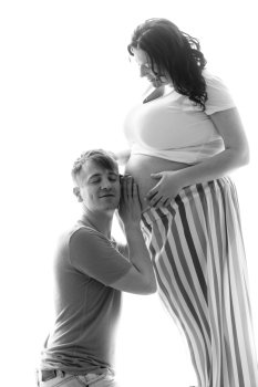 Closeup black and white portrait of handsome man listening to pregnant wife abdomen