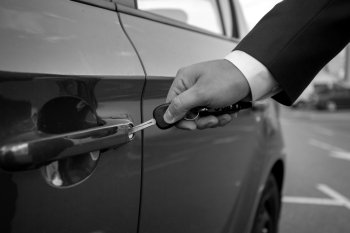 Black and white closeup photo of man inserting car key in the hole