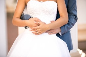Closeup photo of groom hugging slim young bride from back
