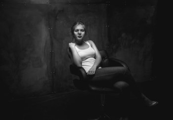 Black and white photo of sexy young woman sitting in chair at dark room