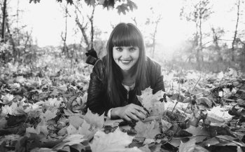 Black and white portrait of smiling woman lying on leaves at autumn forest