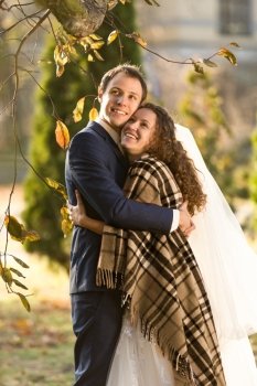 Happy smiling bride and groom hugging under plaid at autumn park