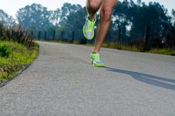 Running sport shoes outdoors in action on country road. Male shoes on young man training. Slight motion blur, focus on back running shoe.