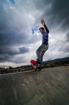 Skateboarder on a grind with dark clouds background at the local skatepark.