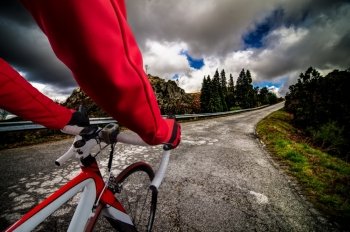 Cyclist on road bike through a asphalt road in the mountains and blue sky with clouds.