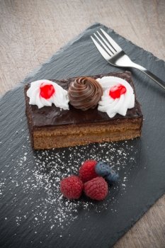 Piece of chocolate cake with berries on dark slate tray.
