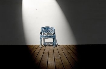 Spotlight on single iron chair on wooden floor