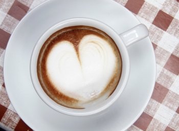 Cup of coffee with heart pattern in a white bowl on a checkered background 