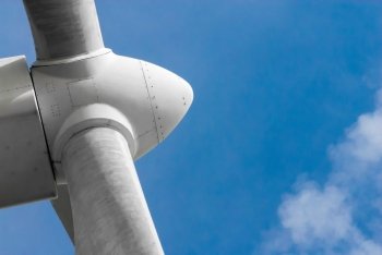 Close-up of white propeller head on wind turbine against blue sky and cloud.
