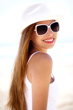 Closeup portrait of young smiling woman with white hat wearing sunglasses