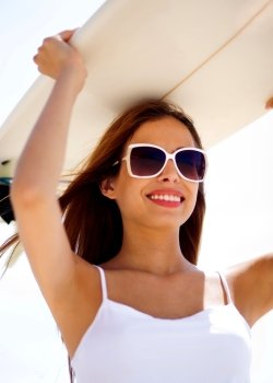 Close portrait of smiling beach woman holding surfboard on her head