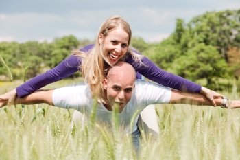 Teenage couple with the lady piggybacking on handsome young man in the grasses