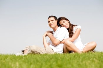 Happy young women with arms around her husband and laying on his shoulder in a park