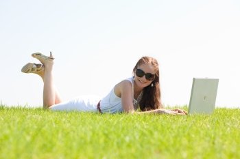 A cute young female lying on the grass in the park using a laptop