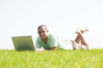 A young men lying on the grass in the park using a laptop