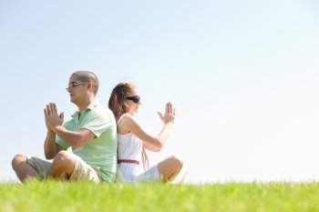 young couple sitting on grass and doing meditating