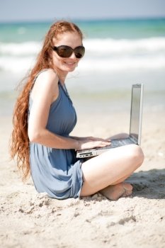Portrait of a woman working with laptop by sitting at the beach sand