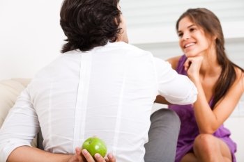 young couple sitting on the sofa,man hiding fruit from his girlfriend