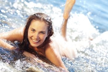 Young tanned woman lying on front and splashing in the surf