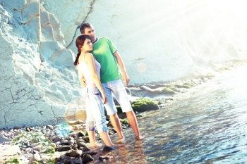 Young couple on the rocky coast standing ankle-deep in water and looking away