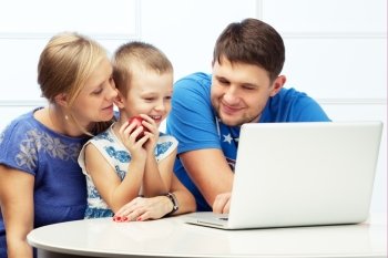 Happy family of three at the table with a computer. Boy holds an apple.