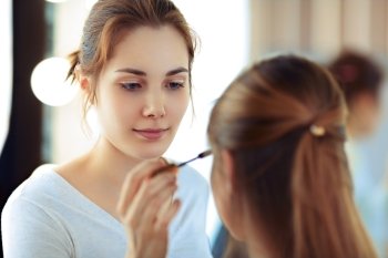 Make-up artist applying mascara on model’s eyelashes, selective focus on MUA