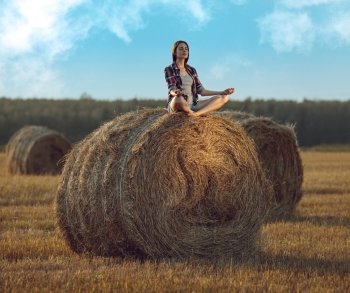 Young woman sitting on a stack of hay and meditating in sunlight 
