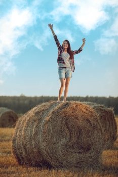 Cheerful young woman standing on a stack of hay in sunlight 