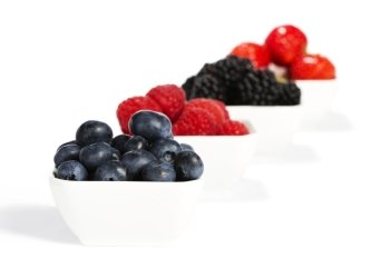 blueberries in a bowl with other berries in background. blueberries in a bowl with other wild berries in background on white background