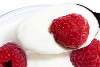 closeup of a raspberry on a spoon with yogurt. closeup of a raspberry on a spoon with yogurt top of other raspberries in a dessert
