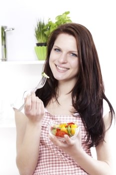 young woman eating mixed salad. young happy woman in kitchen eating mixed salad